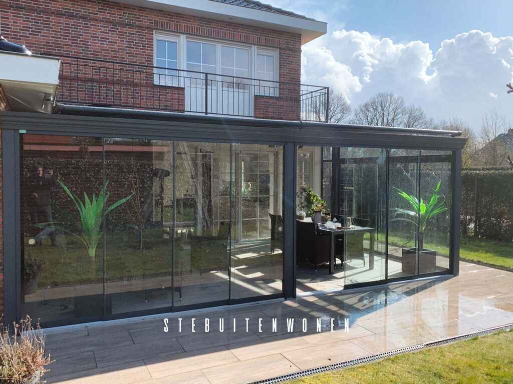 Een overkapping of veranda afgesloten met glazen schuifwanden en een terrasverwarmer of screen