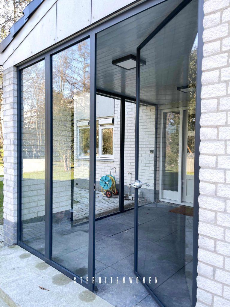 Moderne glazen buitendeur met antracietgrijze aluminium profielen geïnstalleerd in een witte bakstenen buitenmuur